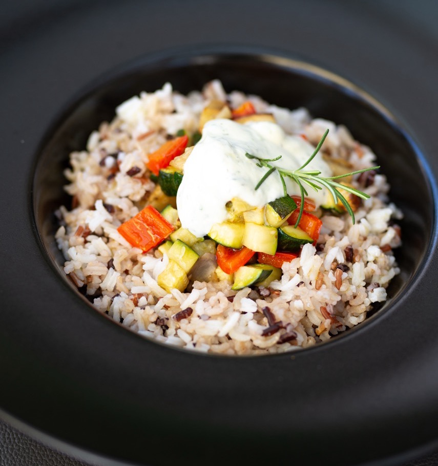 Elegant rice dish with colorful vegetables and creamy garnish in black bowl
